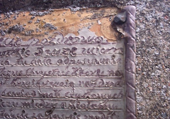 Znikający napis na cokole kapliczki.